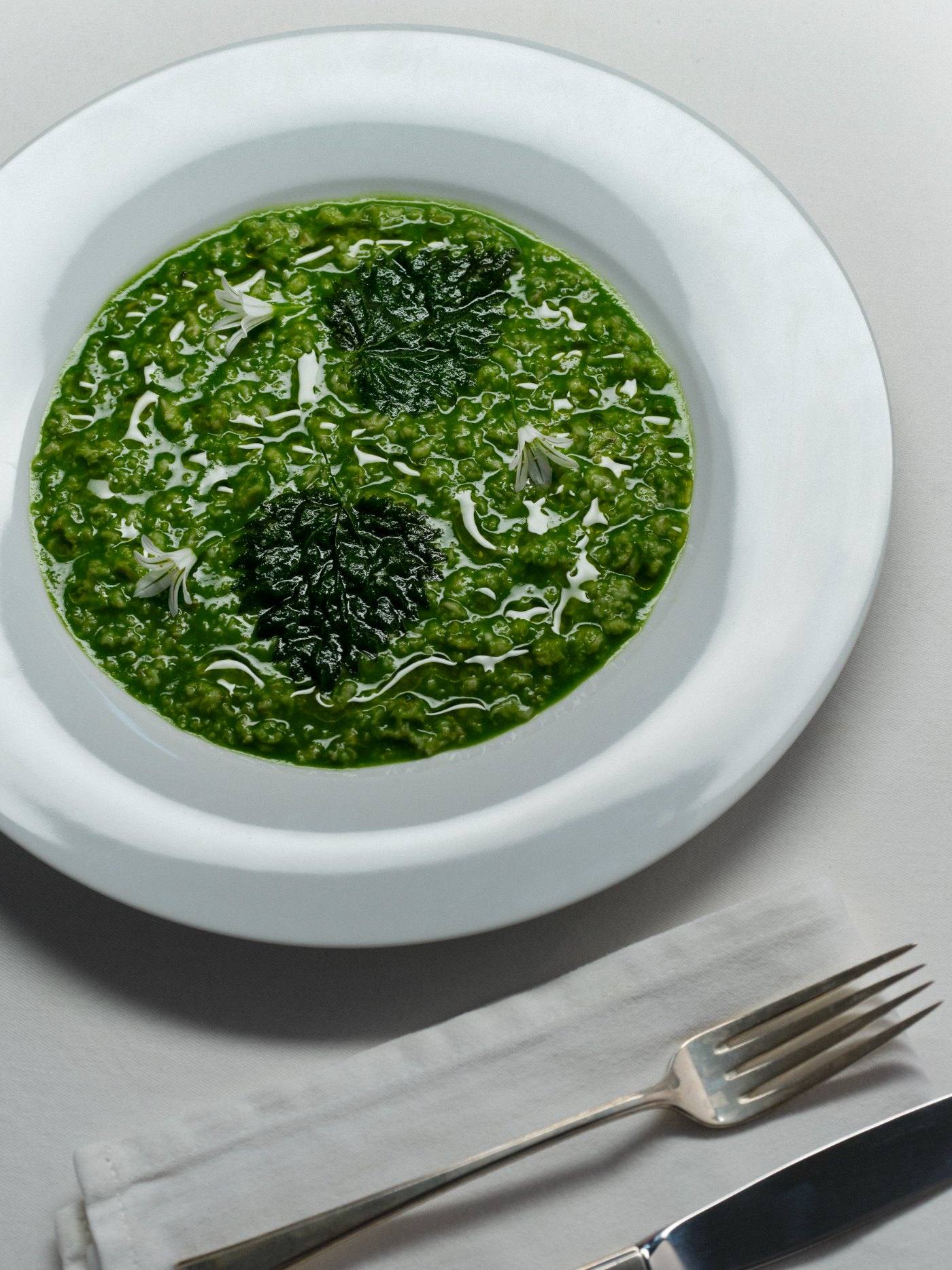 A bowl of bright green nettle risotto on a white plate.